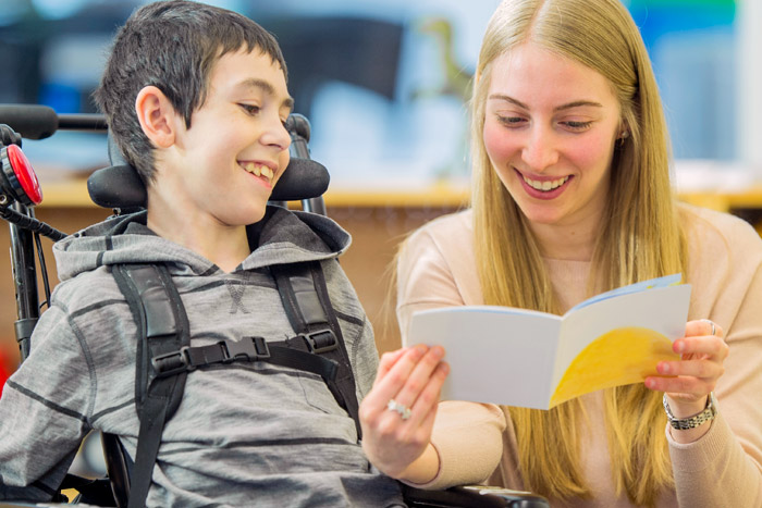 boy in wheelchair smiles while nurse reads him a book